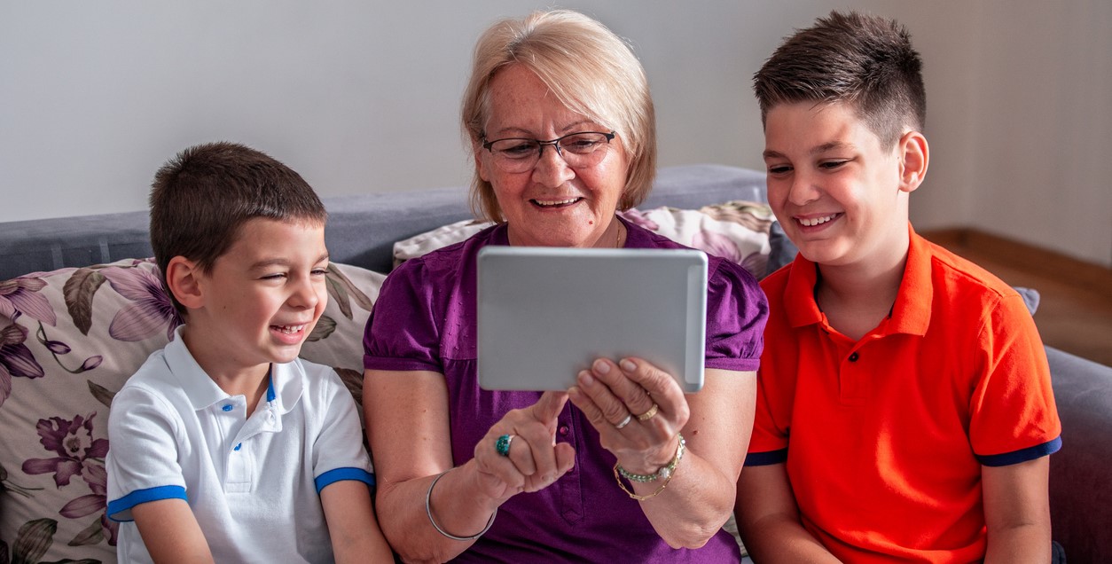 Older lady sitting with iPad with 2 young boys smiling on either side