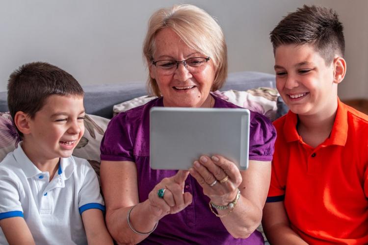 Older lady sitting with iPad with 2 young boys smiling on either side