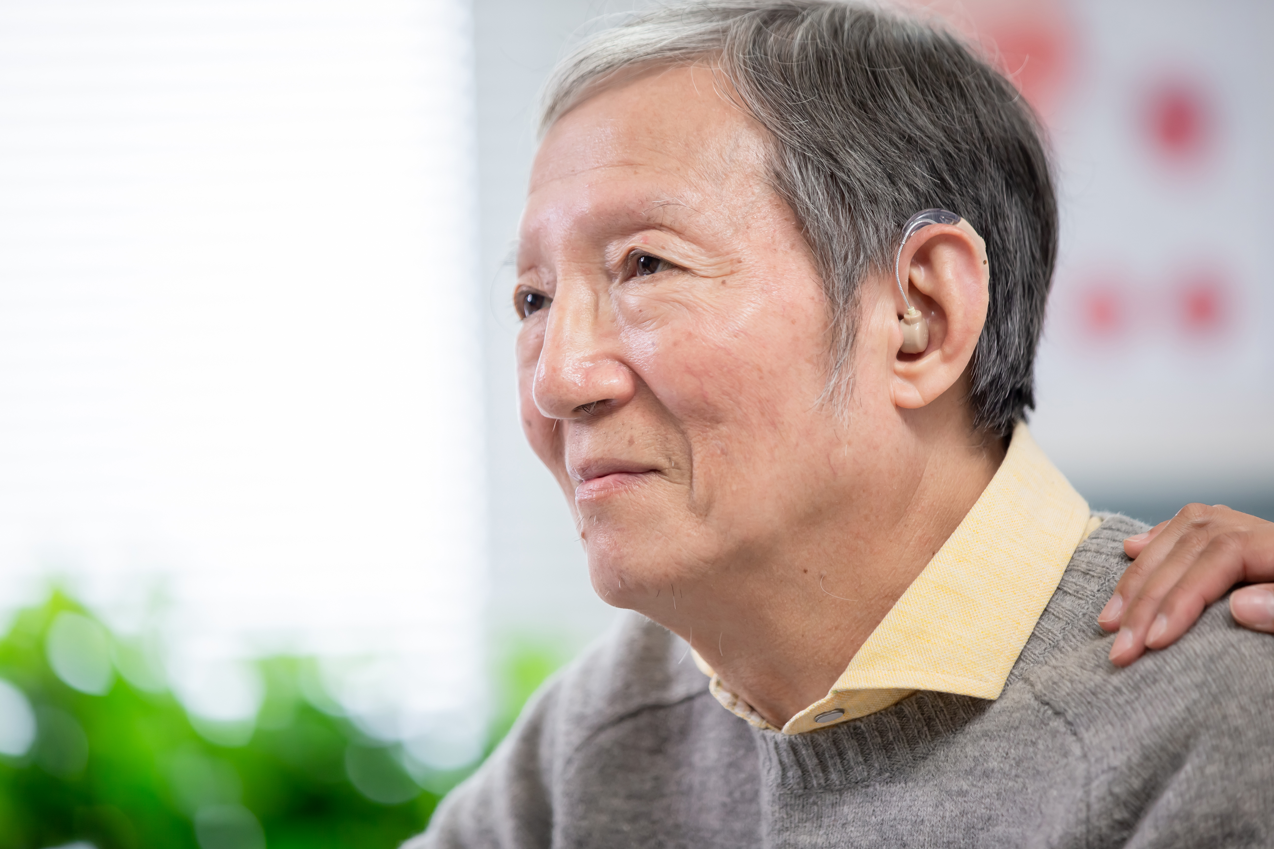 asian man with hearing aid, person's hand on his shoulder
