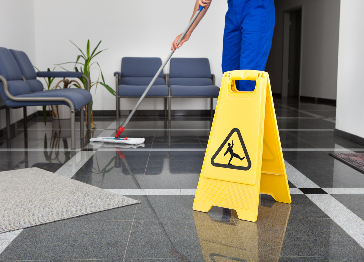 Faceless worker mopping floor with falls warning sign displayed