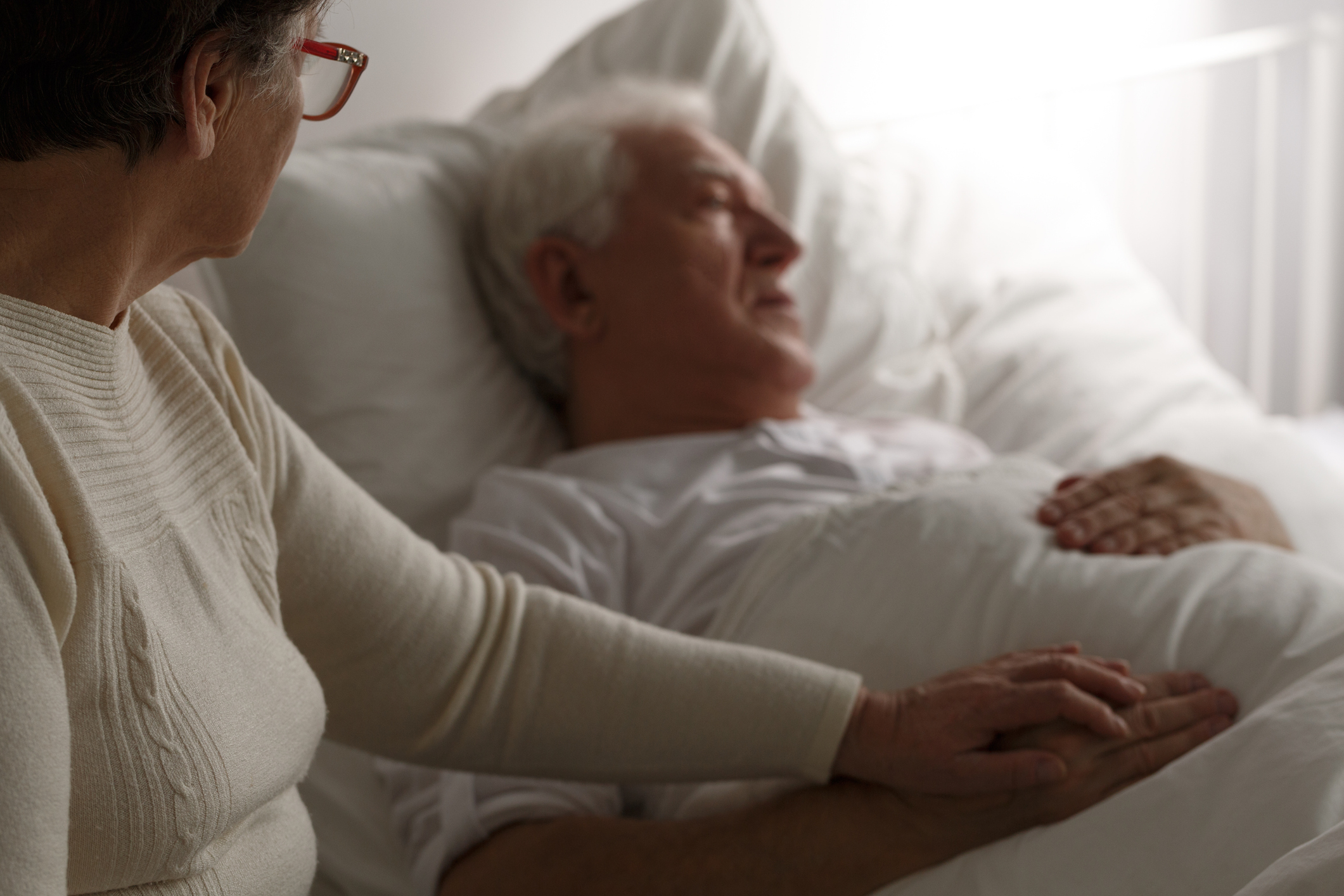 Man lying in bed with wife hand on hand