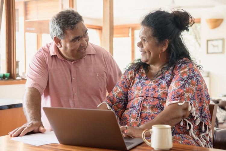 An Aboriginal couple chatting and smiling, the woman is using a laptop