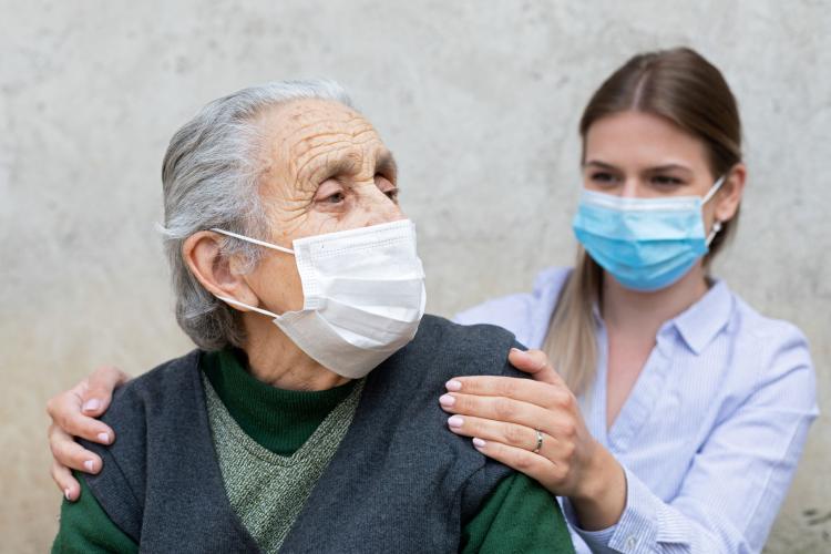 young woman cares for an older woman both wear face masks