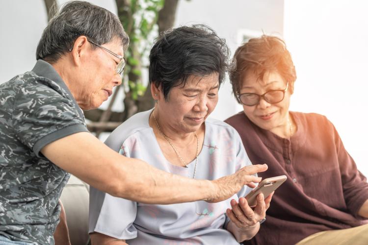 3 older asian people looking at smartphone