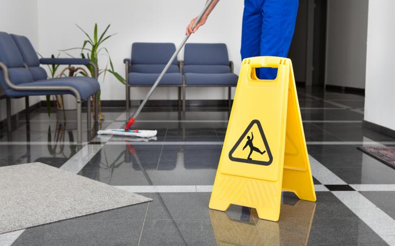 Faceless worker mopping floor with falls warning sign displayed